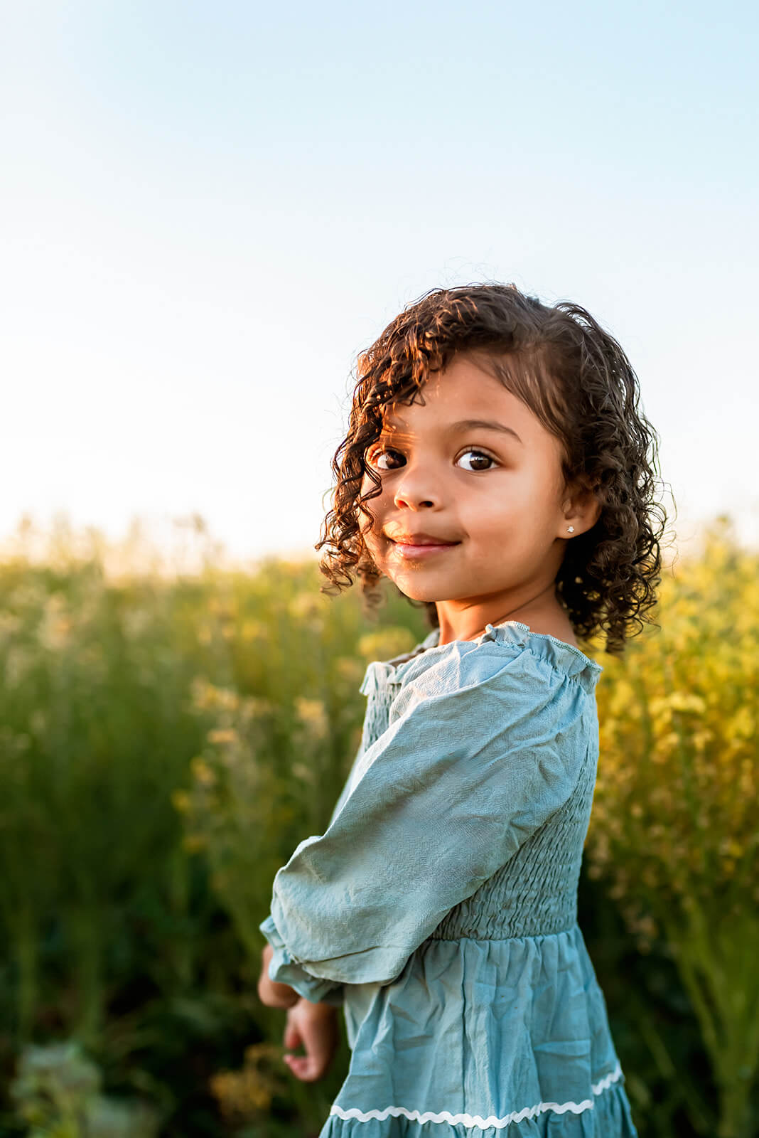 Little girl turns and looks over her shoulder in a field of yellow flowers.
