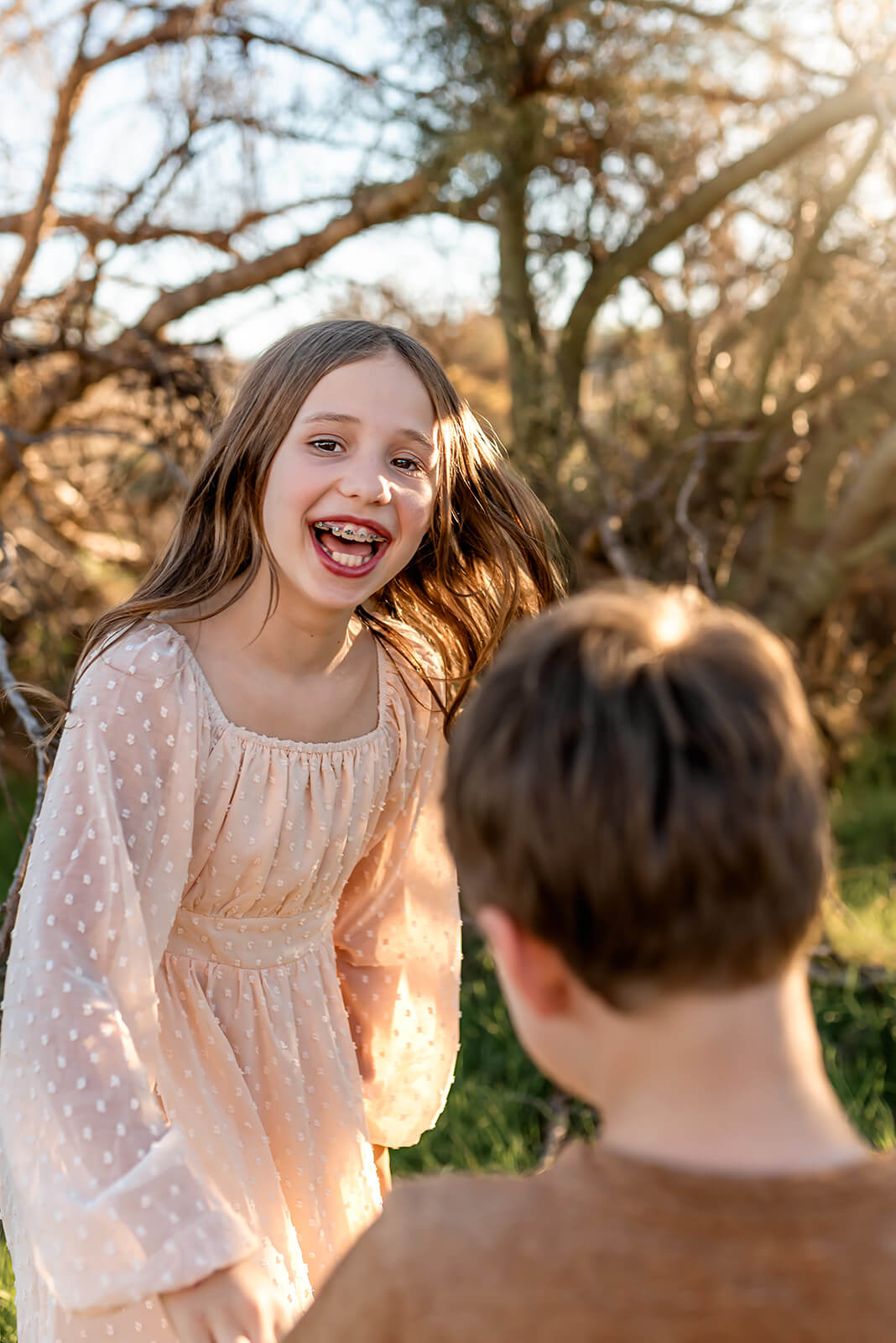 Girl in a cream colored dress laughs while her little brother stands in front of her.