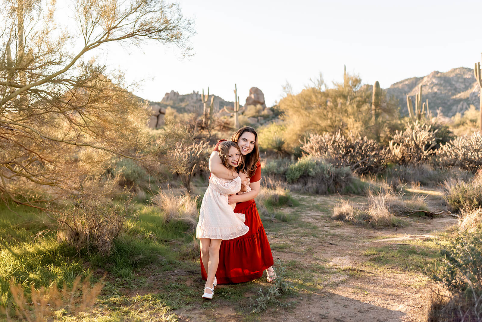 Mom and daughter dance in the desert in flowing dresses.