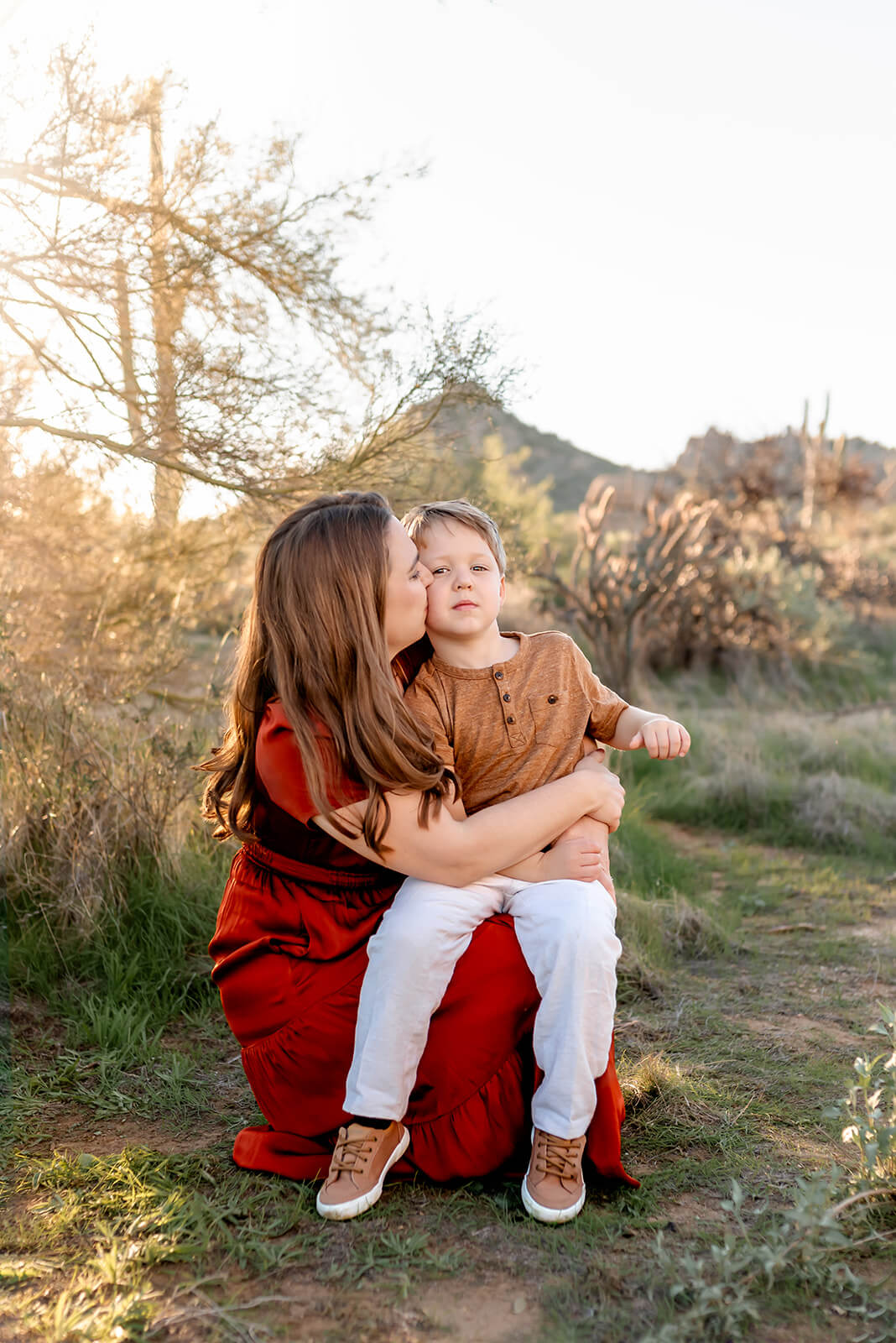 Mom holds her son on her lap and gives him a kiss during a golden hour desert flower session.