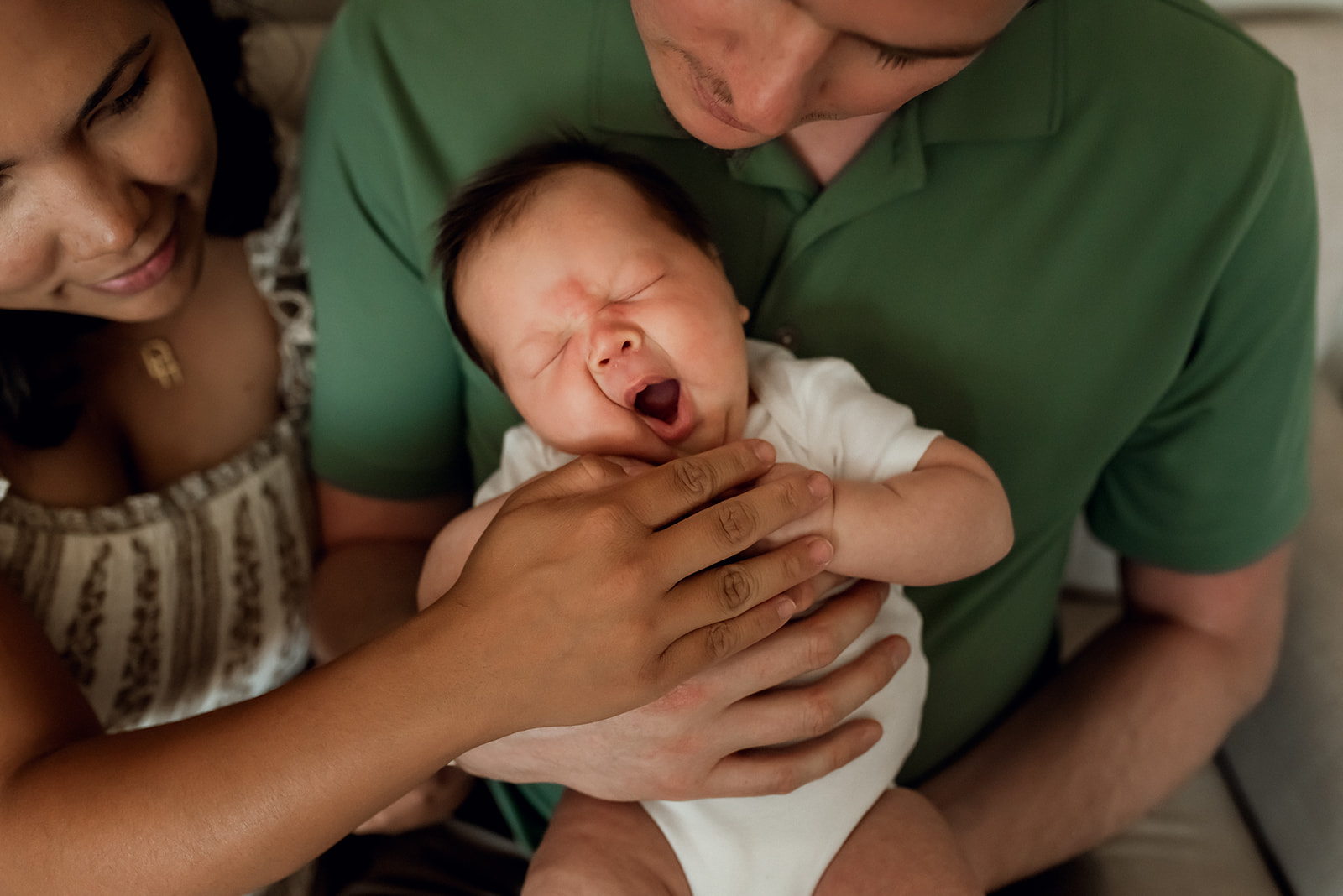 Newborn baby boy is held in his father's arms and embraced by his mother while he yawns.