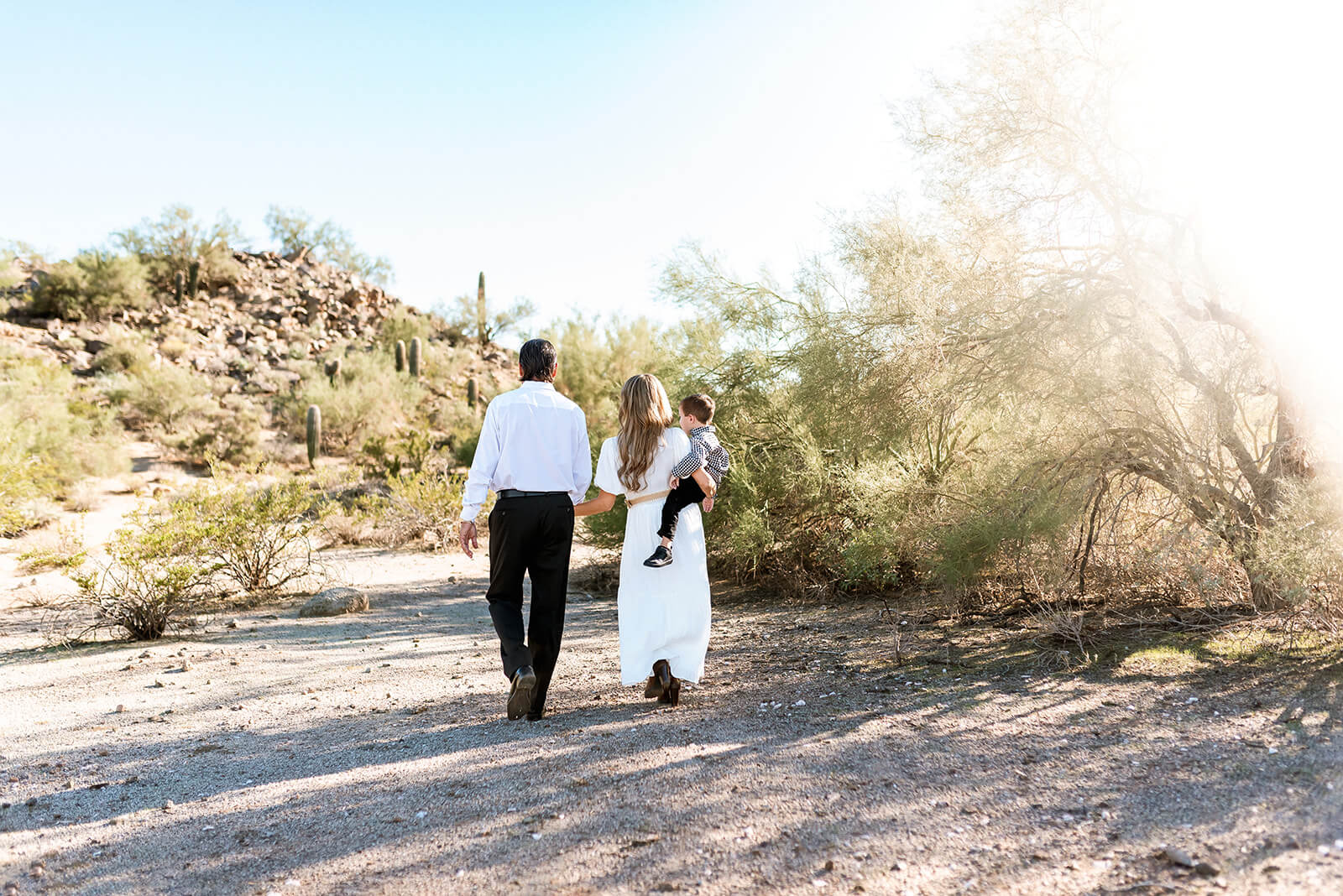 Family of three walk away from the camera in a glowy sunset family photo session.