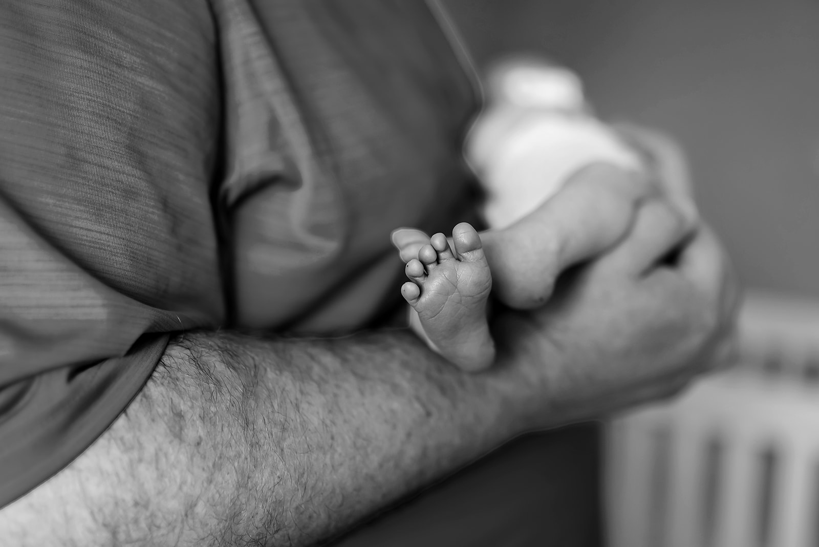 Black and white photo of the feet of a newborn baby as she's held in her dad's arms.