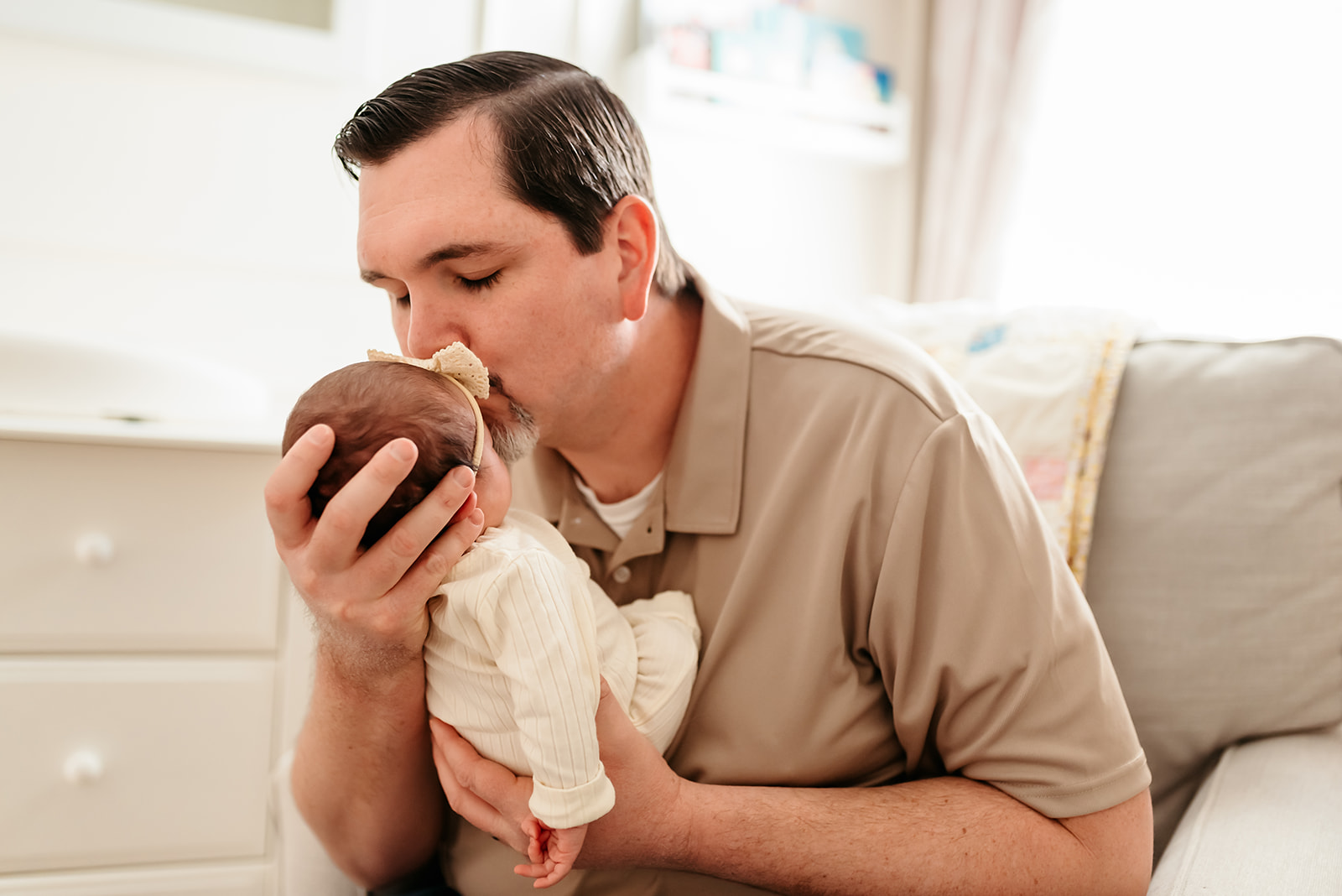 Father holds newborn baby girl up in his arms to kiss her on the forehead.
