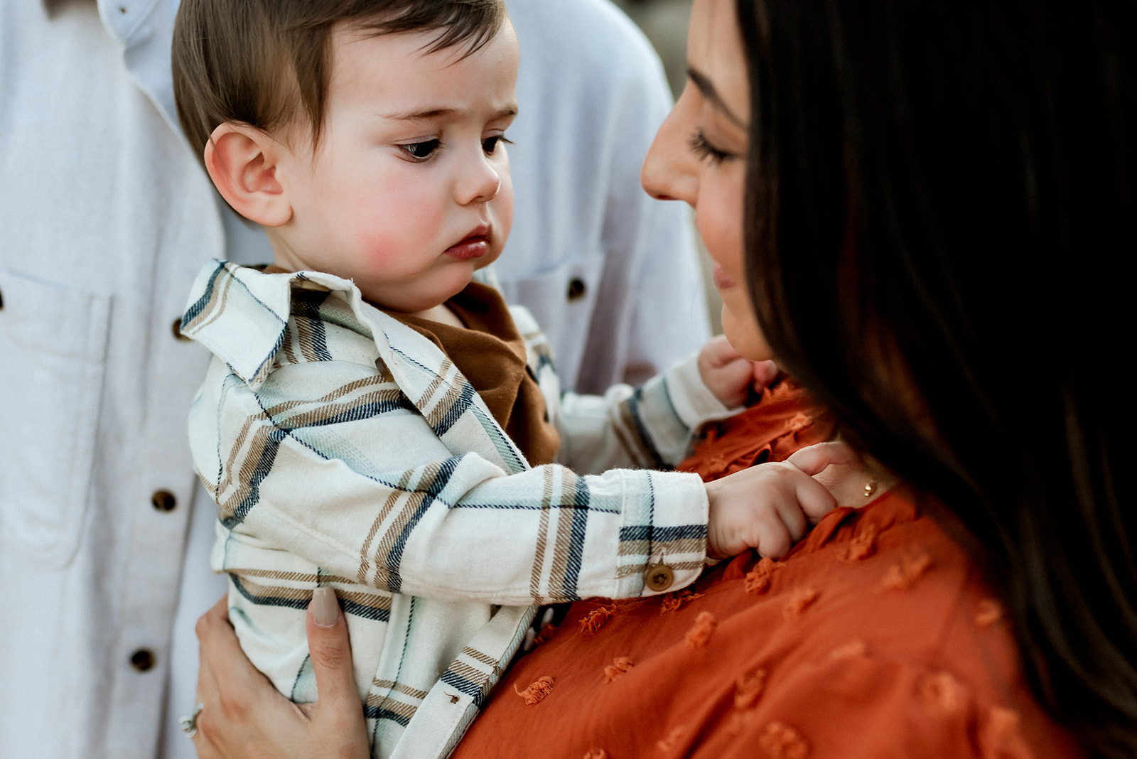 Baby boy is held by his mom and plays with her necklace as she smiles at him.