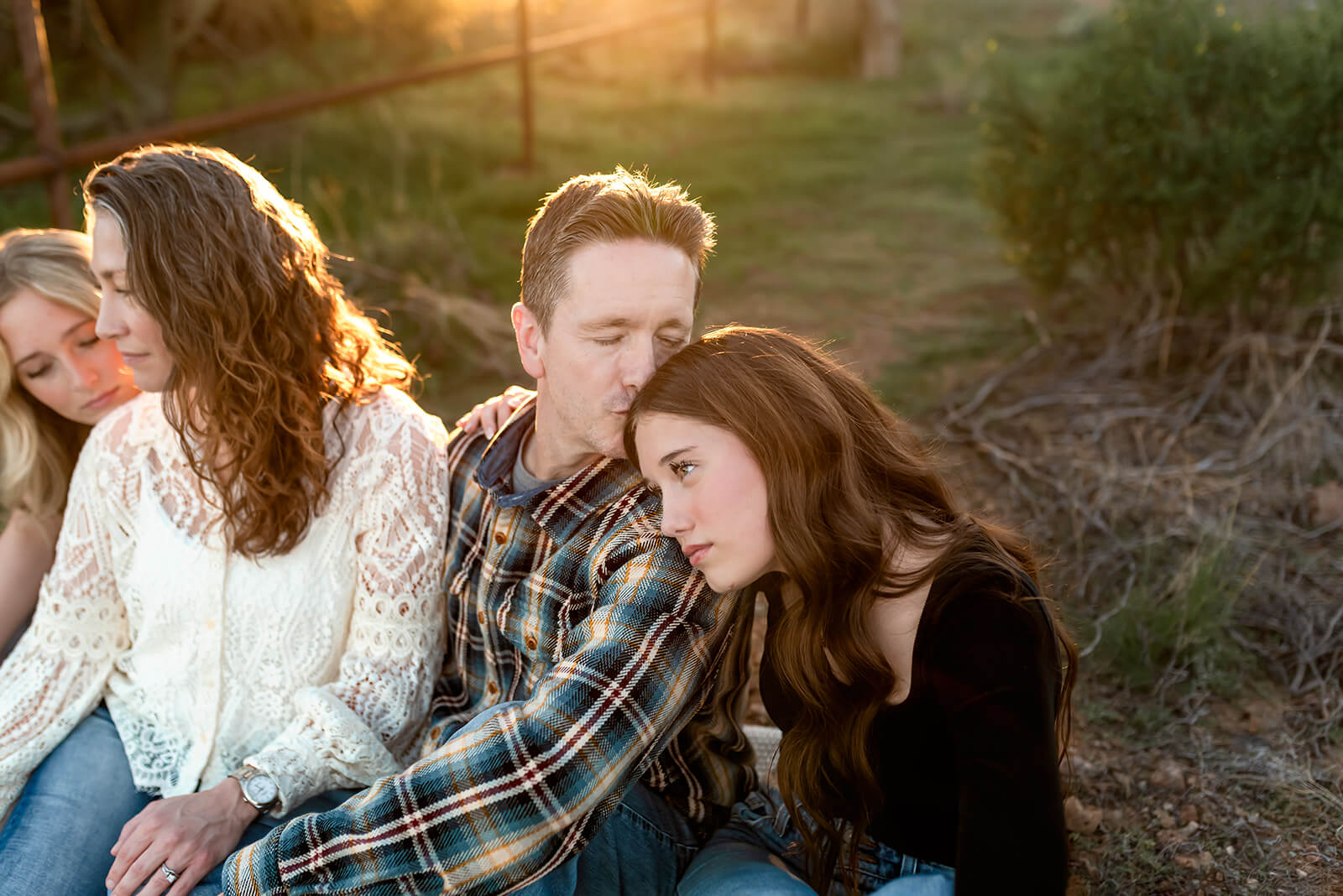 Teenage girls sit with their parents in the desert, while dad kisses his daughter's head.