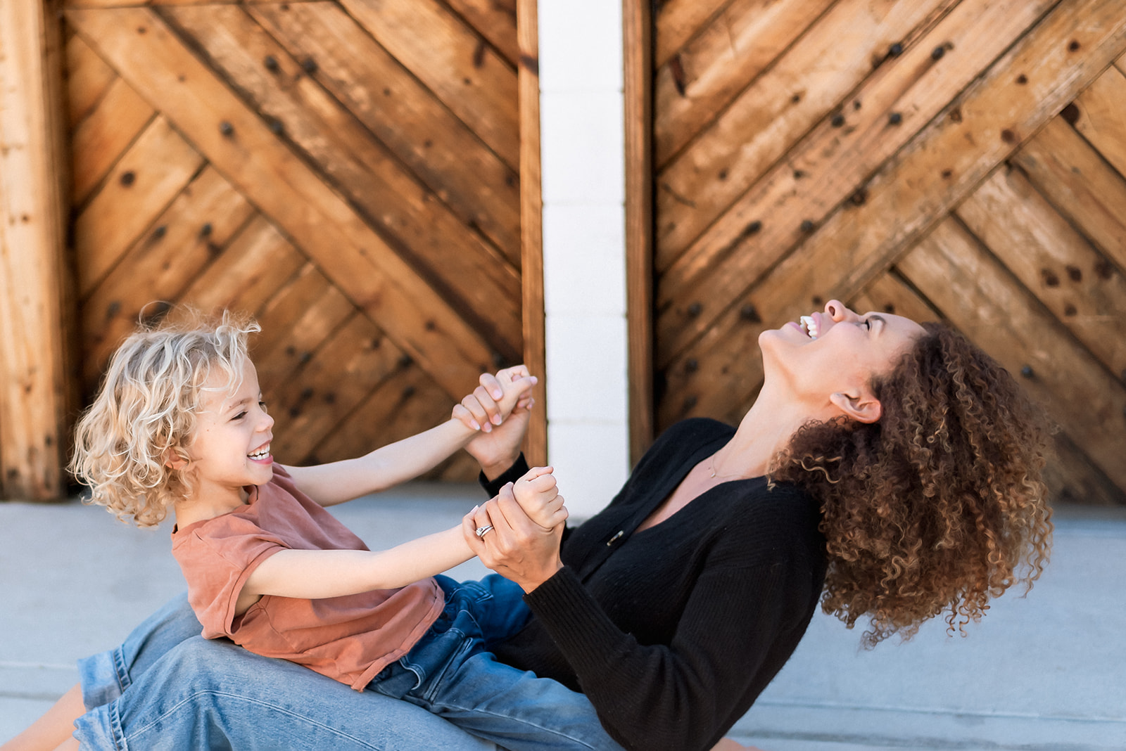 Little boy with curly hair sits on his mom's lap as the rock back and forth on the ground laughing joyously.