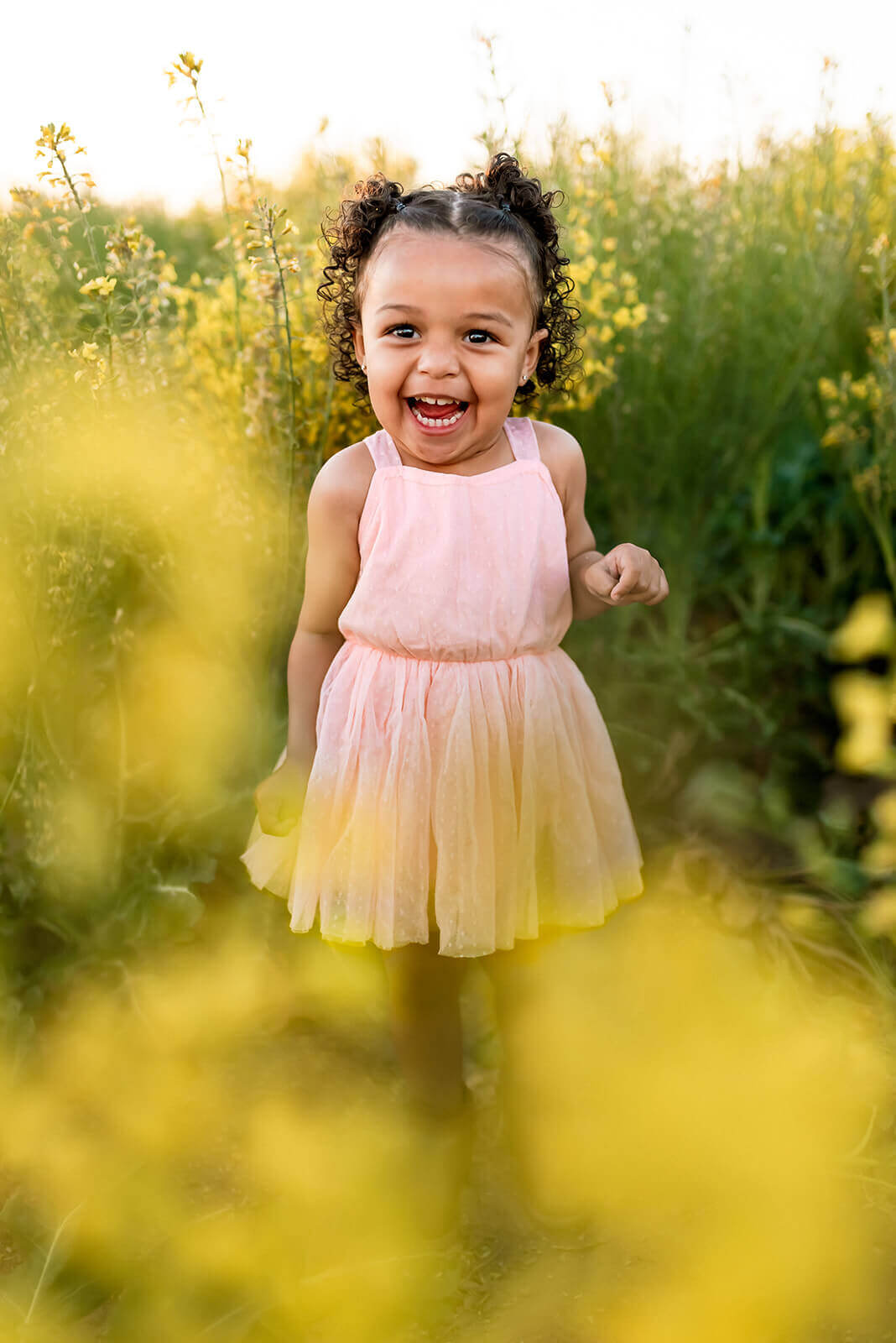 Little girl smiles and laughs joyfully surrounded by a field of yellow flowers.