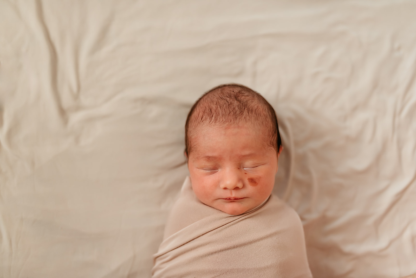 Newborn baby girl swaddled in a beige blanket against a beige backdrop.