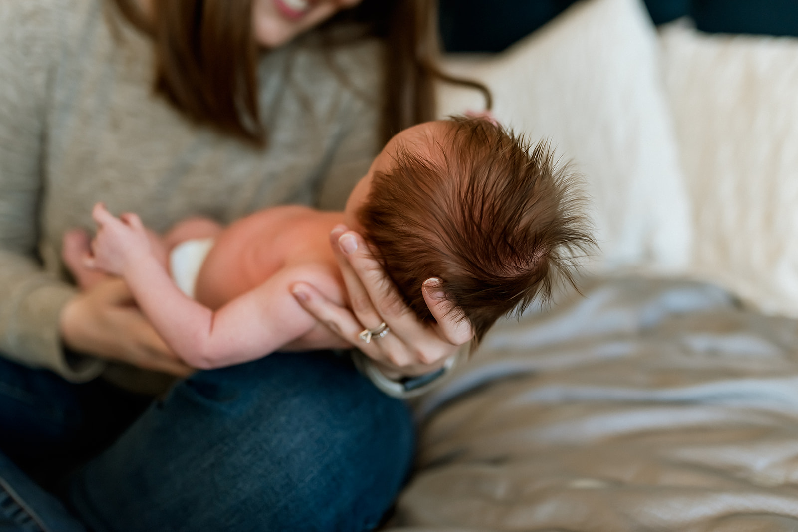 Parent sits on a bed and holds their newborn baby. Details of the baby's hair are shown.