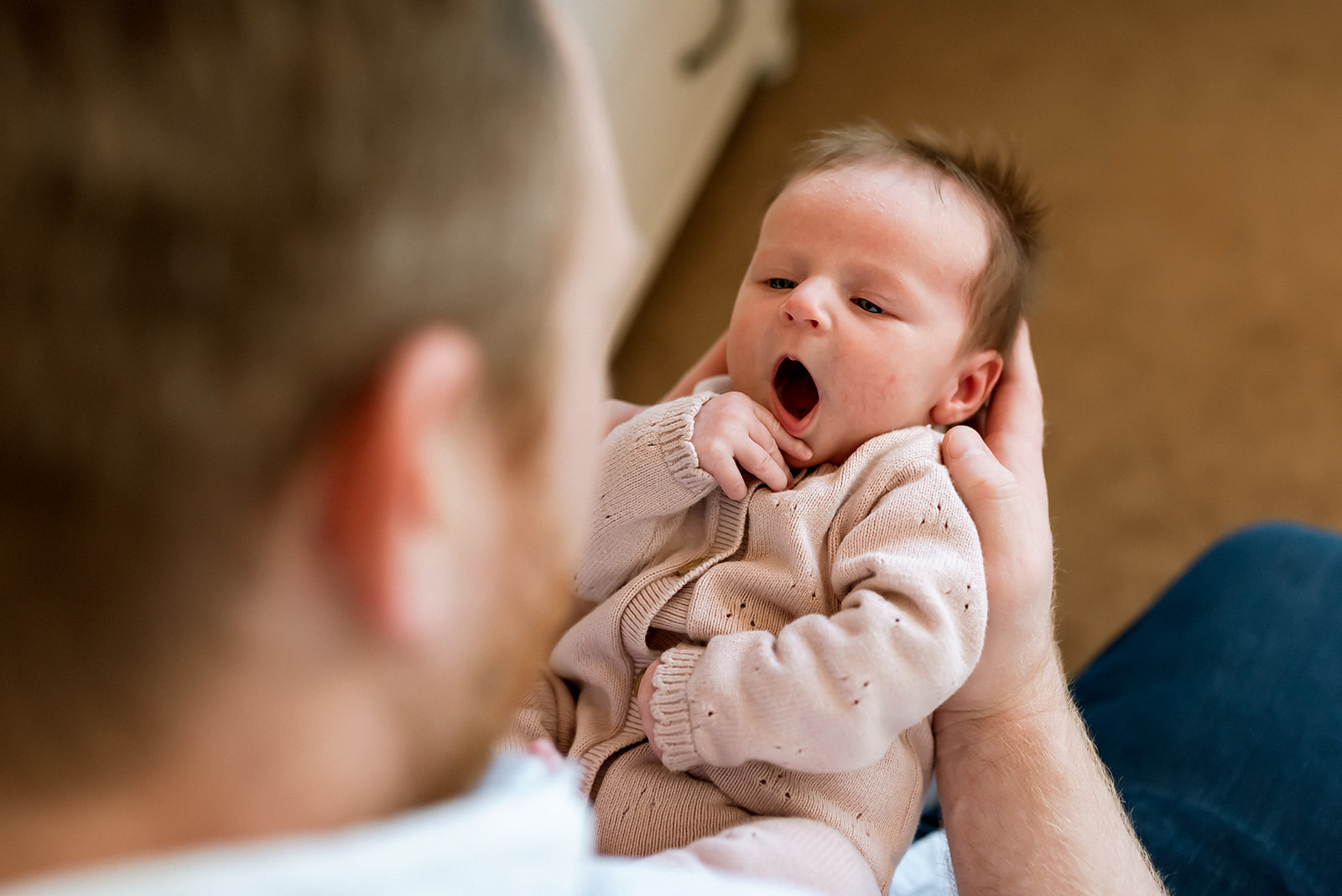 Dad holds newborn baby in his arms and looks at her while she yawns.