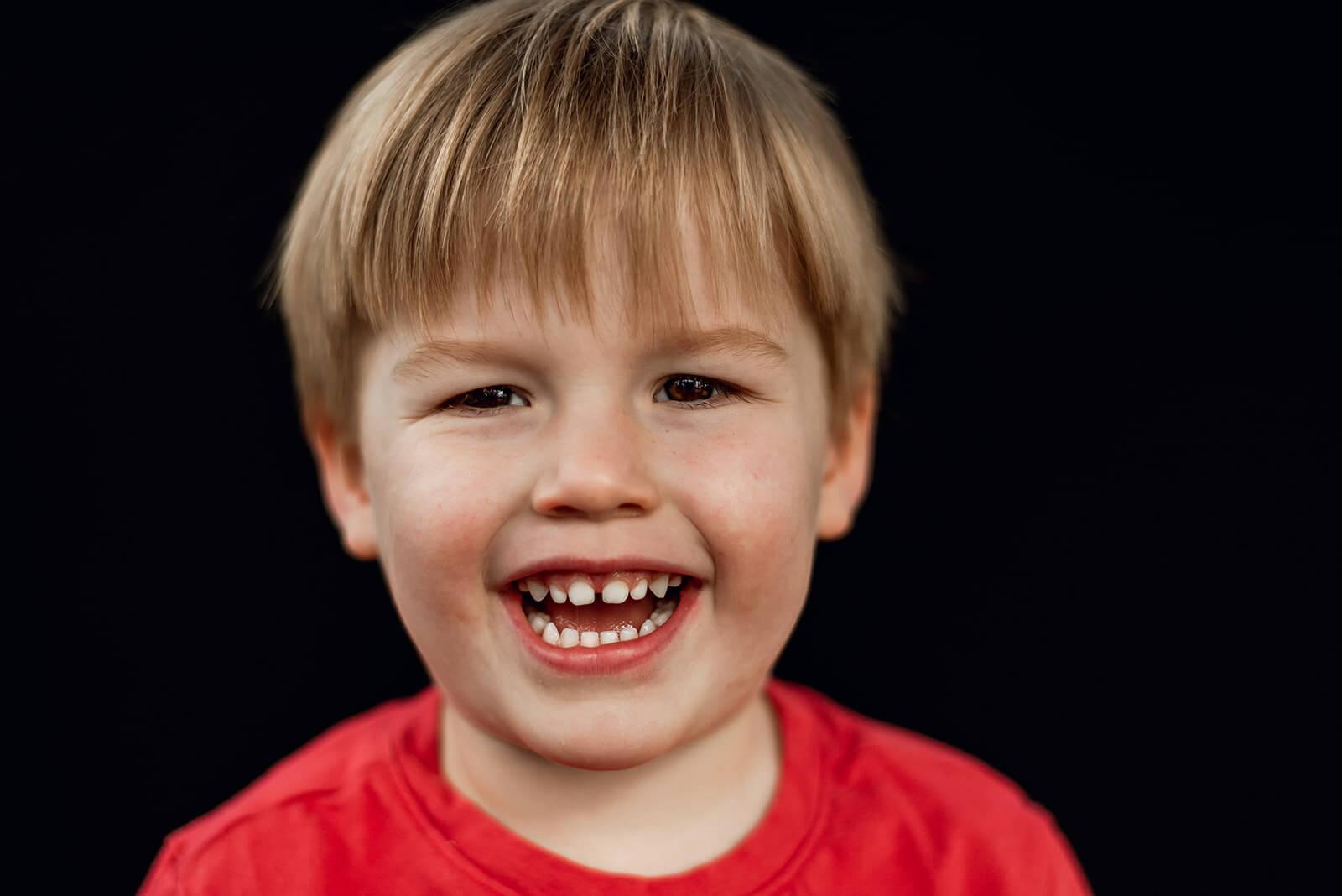 Little boy smiles laughing wearing a red shirt.