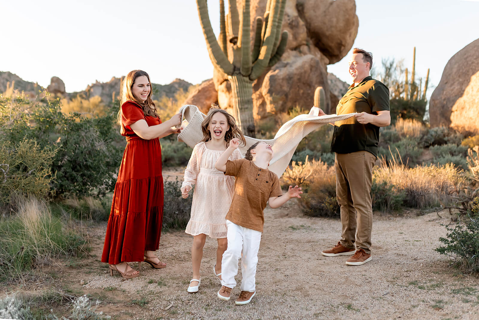 Kids run joyfully under a blanket their parents are throwing into the air.