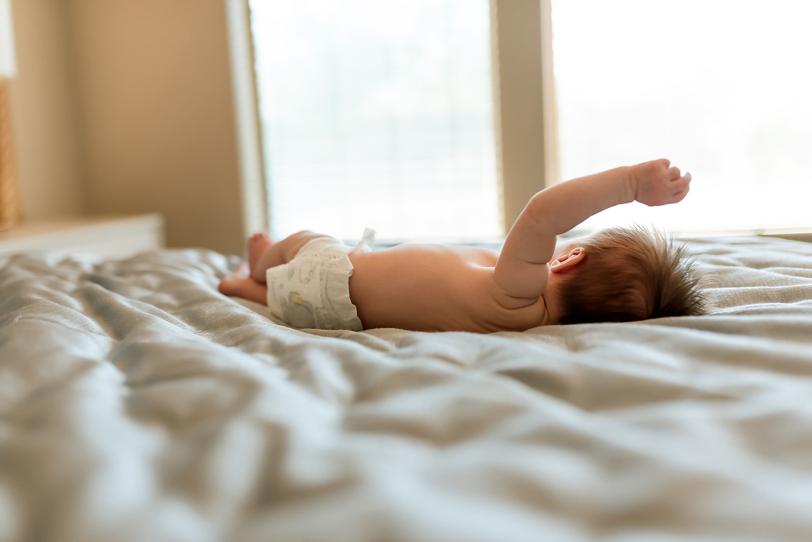 Newborn baby lies a baby moving her arms and legs with window light in the background
