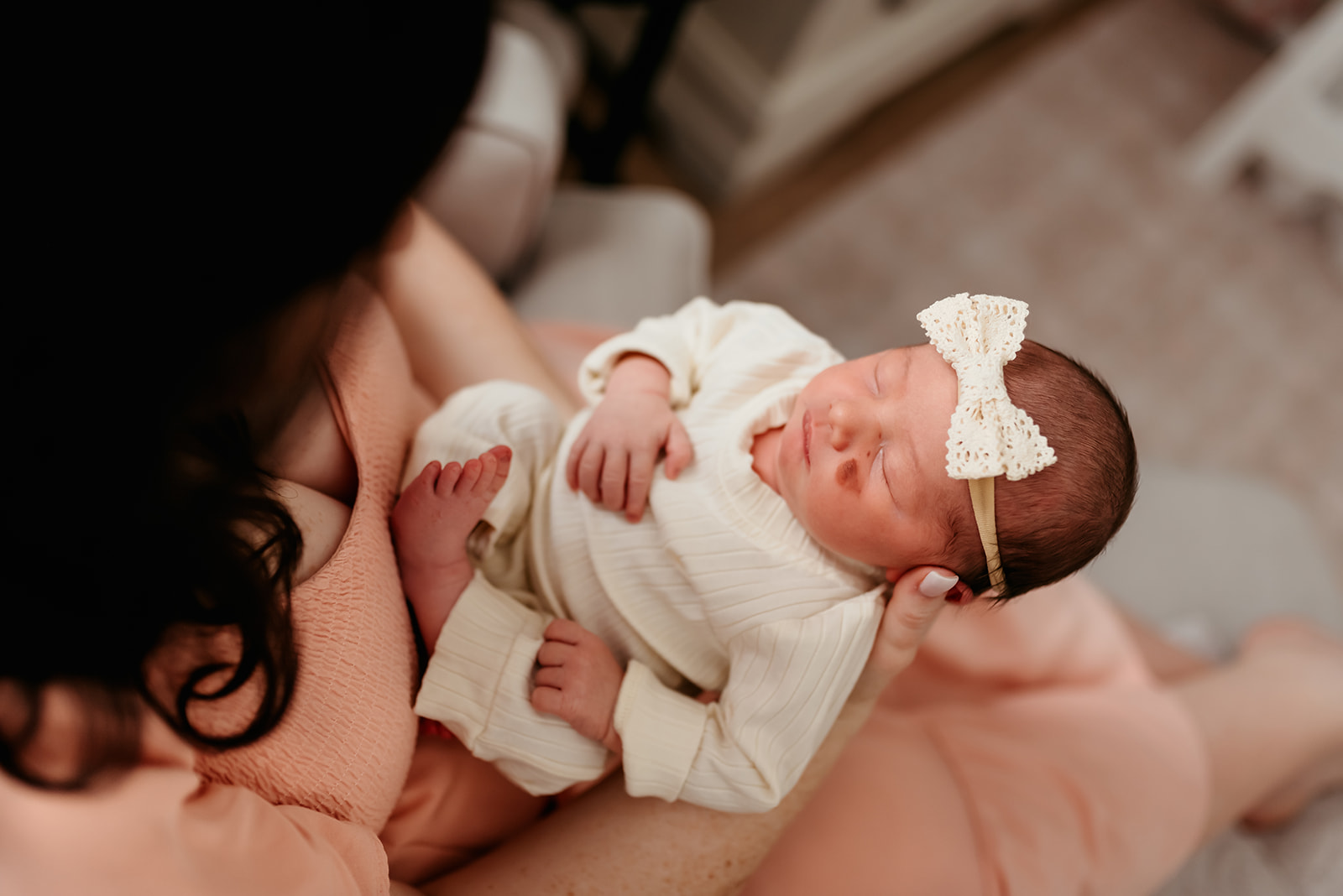 Mom holds newborn baby girl in her lap so you can see the details of her face and little hands