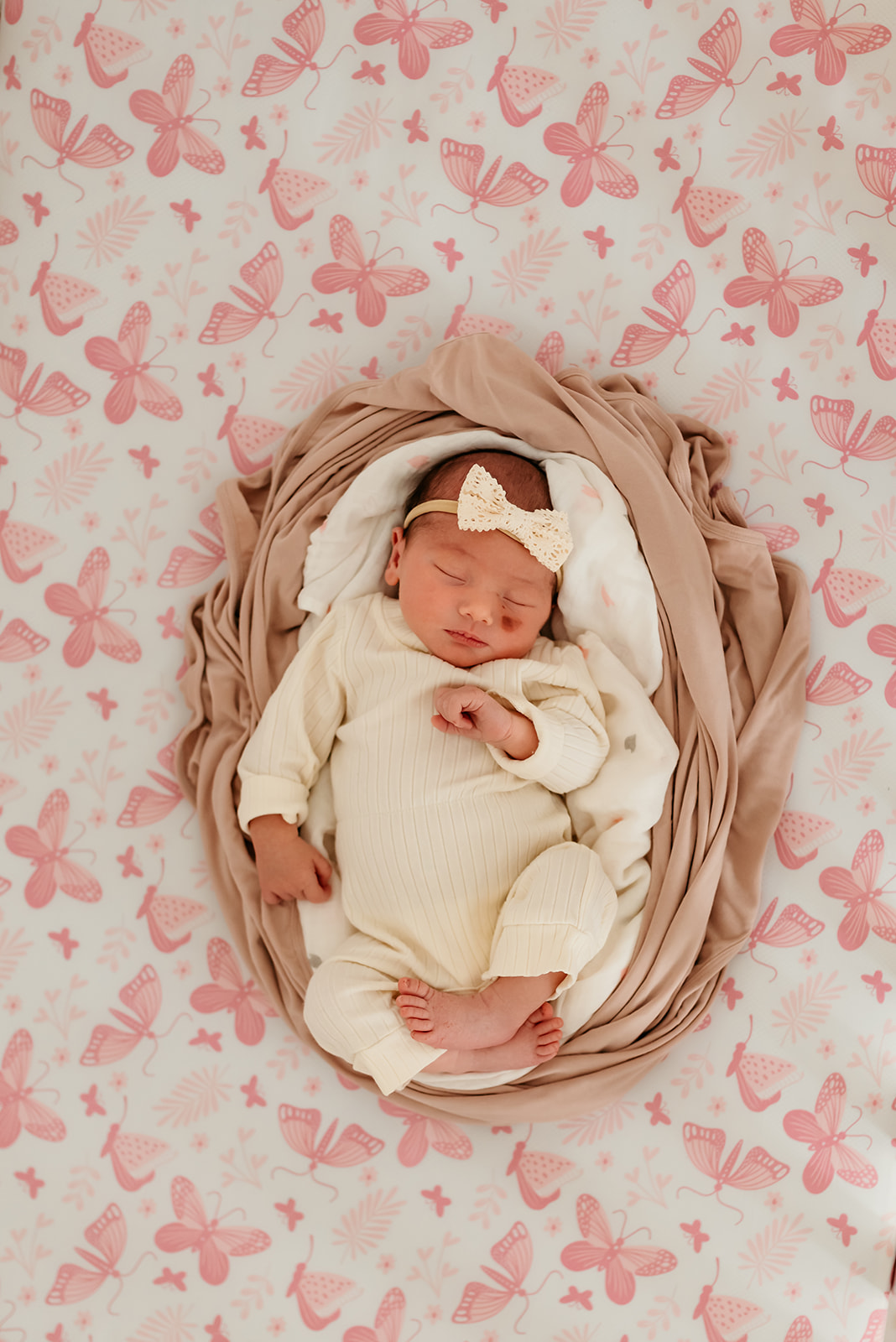 Newborn baby rests in a nest of blankets with a backdrop of pink butterflies.