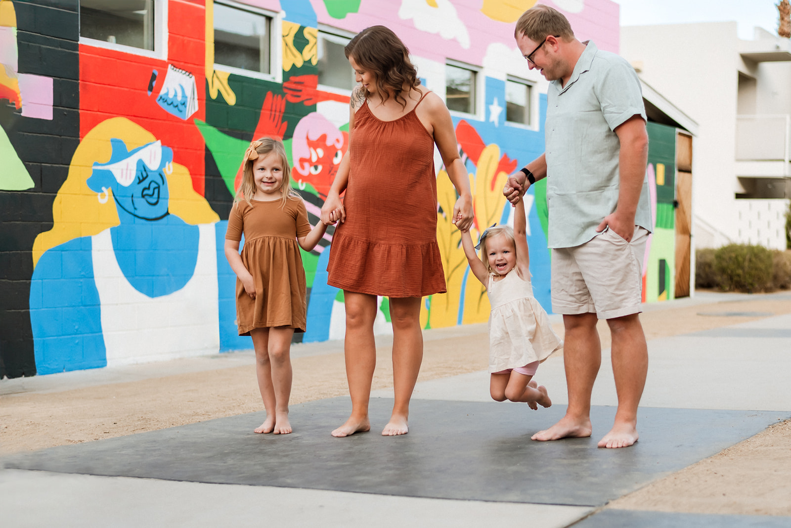 Family of four walks holding hands looking at each other and little girl is swung between mom and dad.