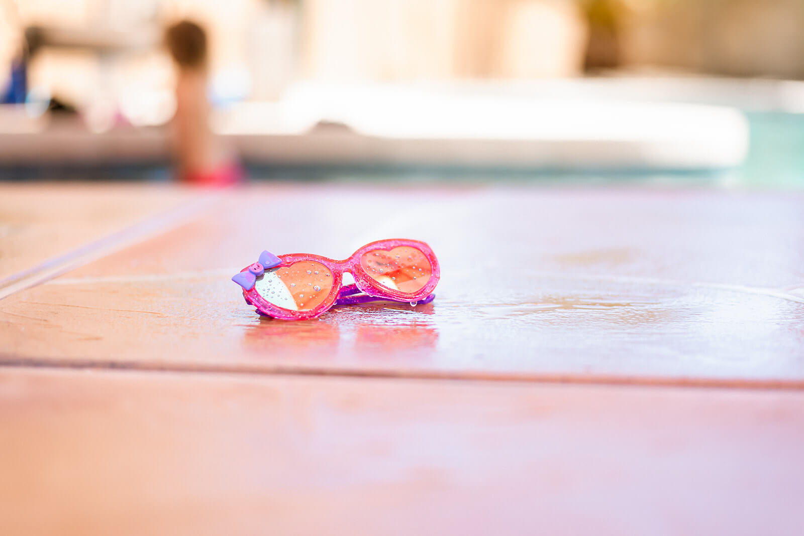 Pink mirrored sunglasses sit on a wet cool deck next to Phoenix pool