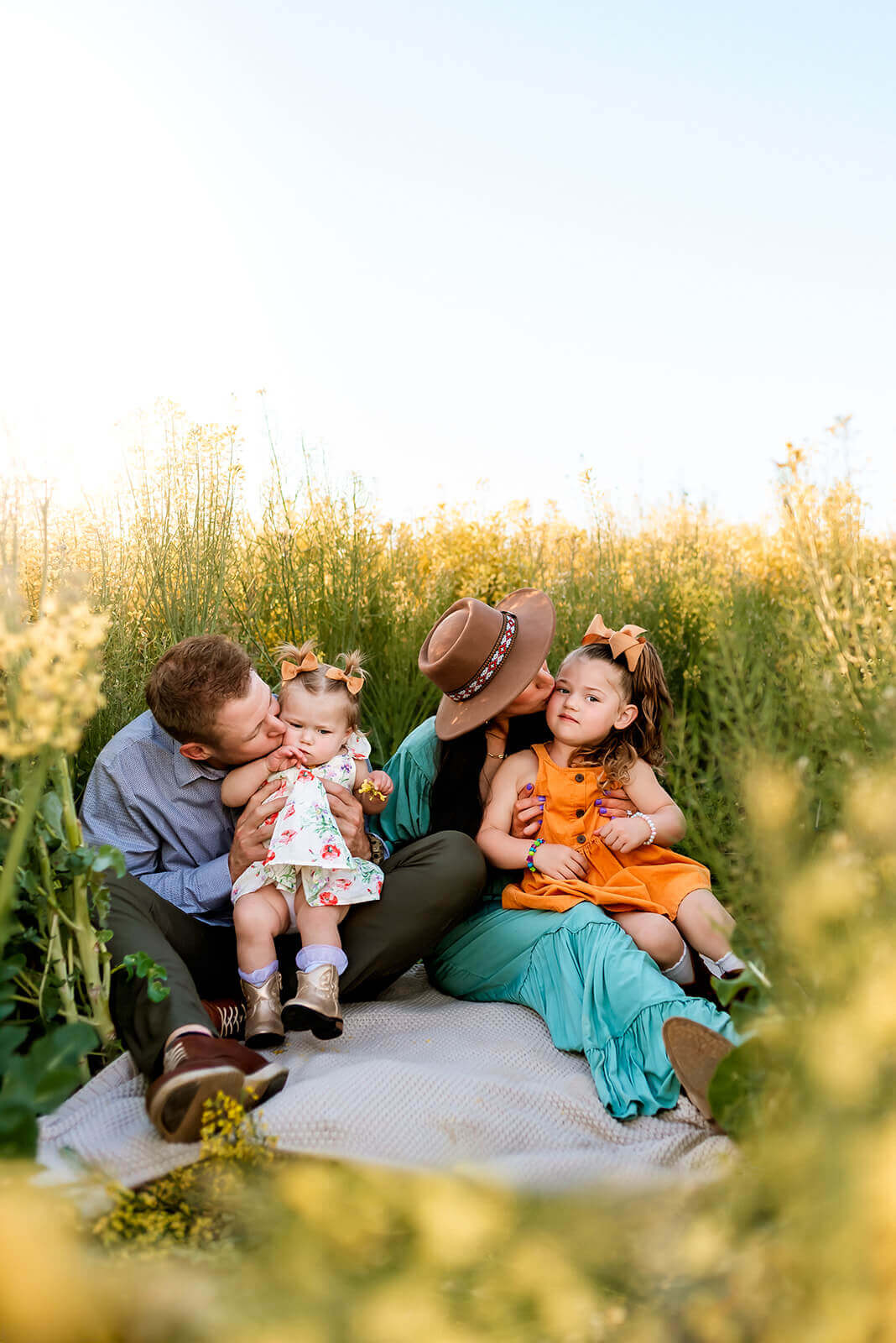 Family of four sit amongst a field of flowers loving on each other during a golden hour photo session