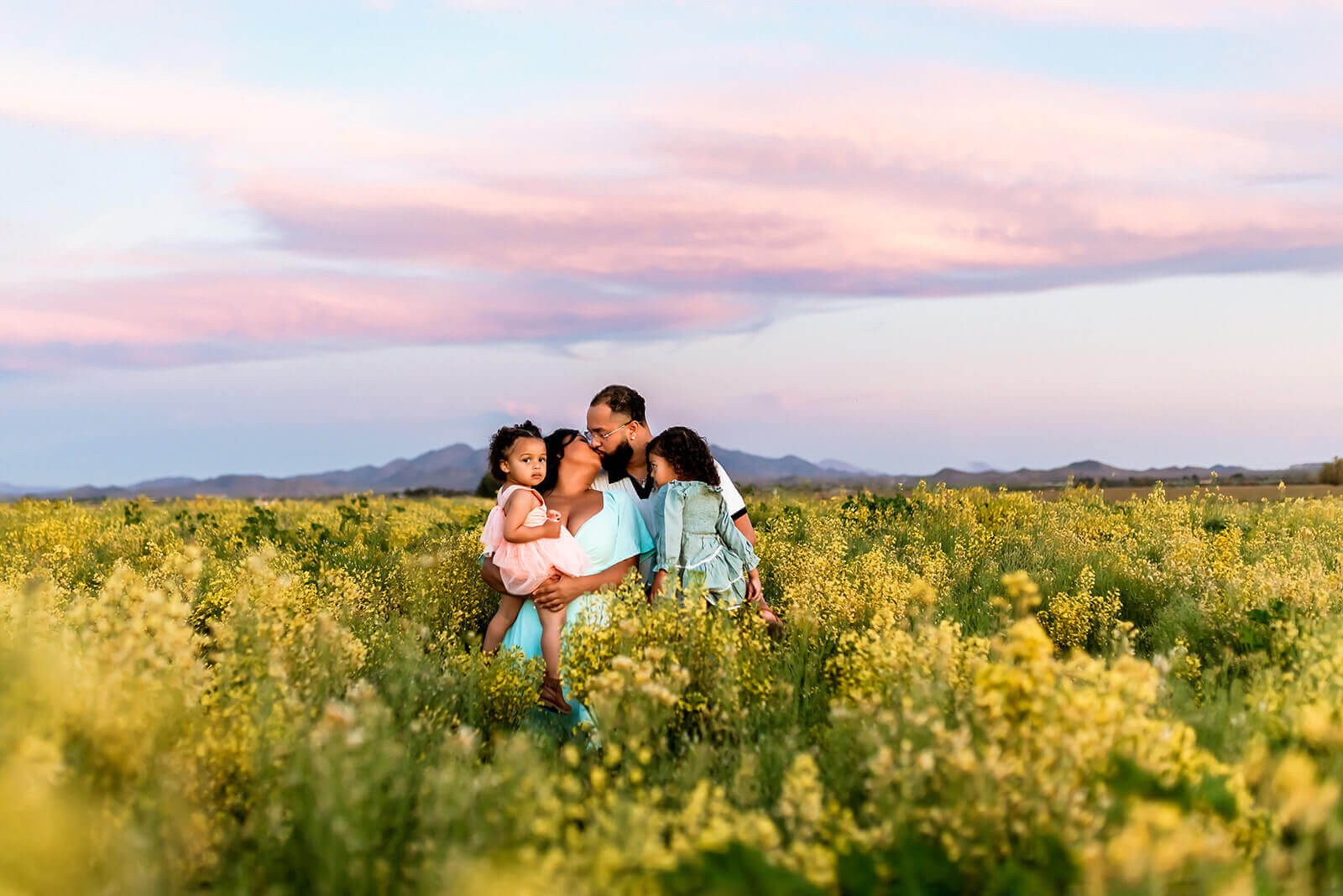 Golden hour photo in Buckeye where a family of four stands in a field of flowers with a cotton candy sunset behind them.