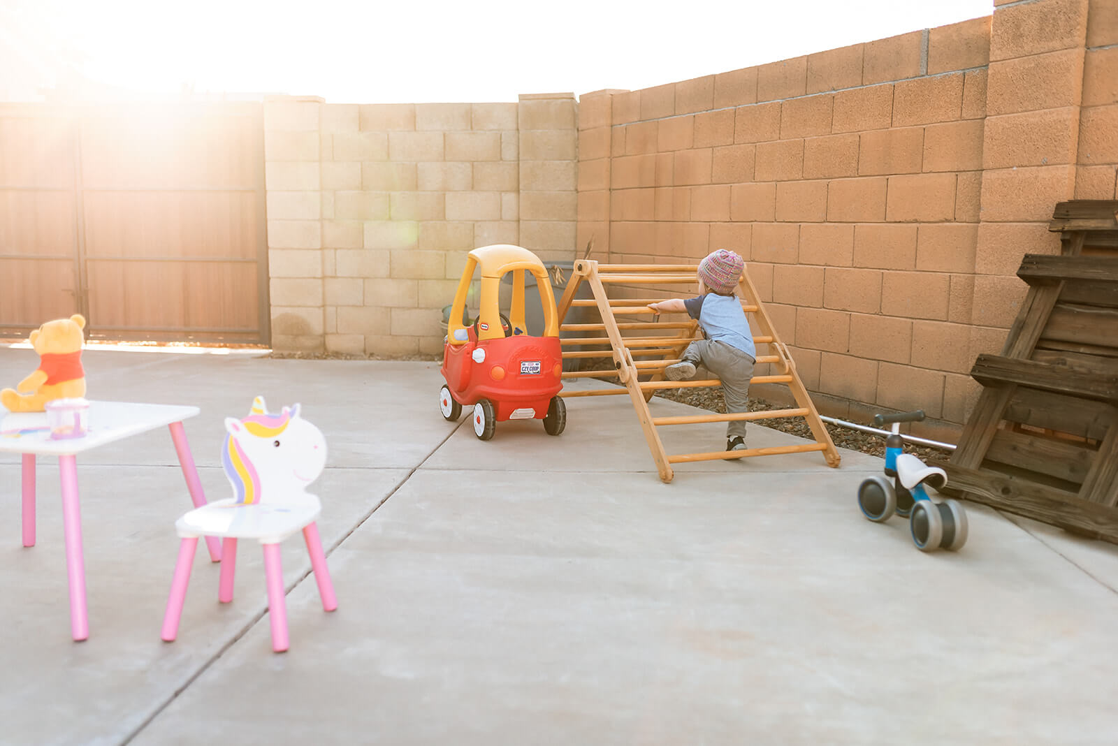 Little boy climbs on climbing triangle with toys around the yard and golden light